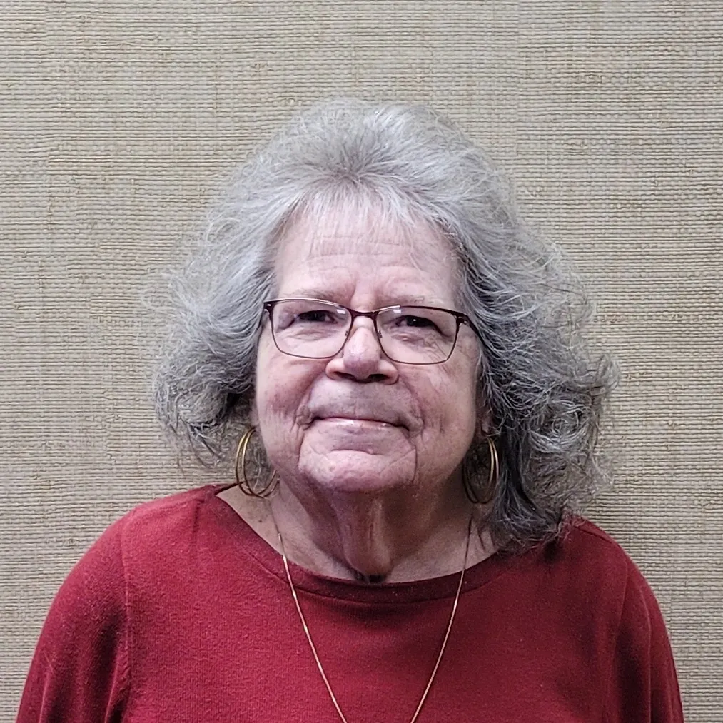A woman with grey hair wearing glasses and red shirt.